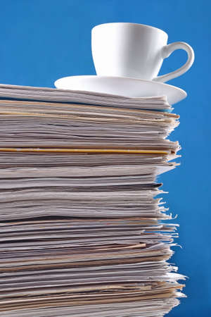 Cup on a pile of papers against a blue backgroundの写真素材