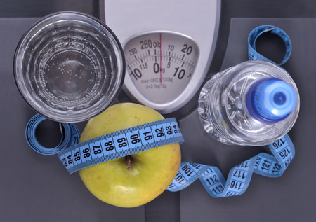 Bottle of water green apple glass of water and measuring tape on a scaleの写真素材