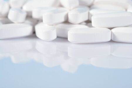 Heap of white pills close up on a blue backgroundの写真素材