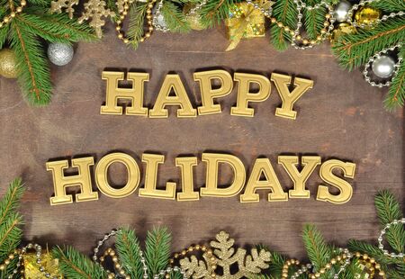 Happy holidays golden text and spruce branch and Christmas decorations on a wooden backgroundの写真素材