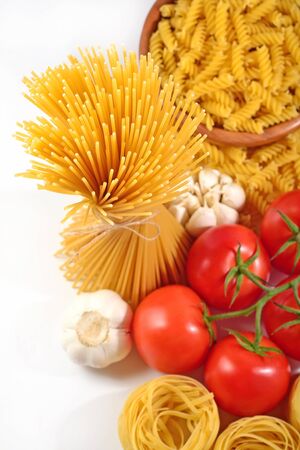 Uncooked Italian pasta, ripe tomatoes branch and garlic on a white backgroundの写真素材
