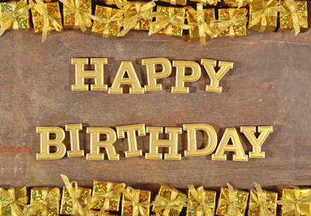 Happy birthday golden text and golden gifts on a wooden backgroundの写真素材