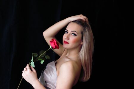 blond woman in dress on black background with a roseの写真素材