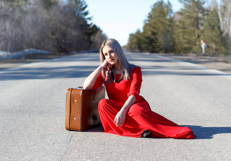 beauty young woman in red dress on road with red luggageの写真素材