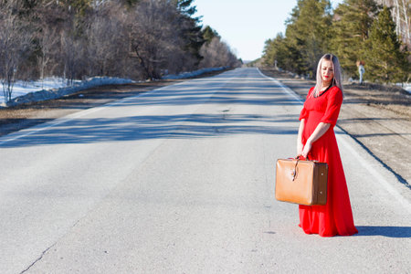 beauty young woman in red dress on road with red luggageの写真素材