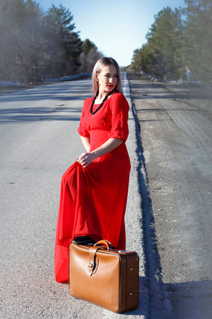 beauty young woman in red dress on road with red luggageの写真素材