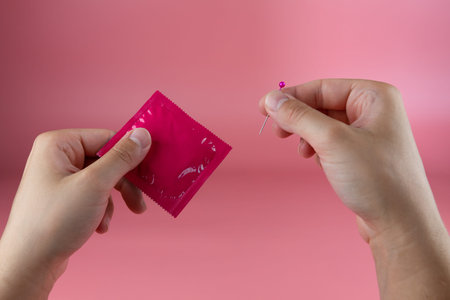 Young girls hands poking a hole in a condom with a needle, infidelity concept, getting pregnantの写真素材