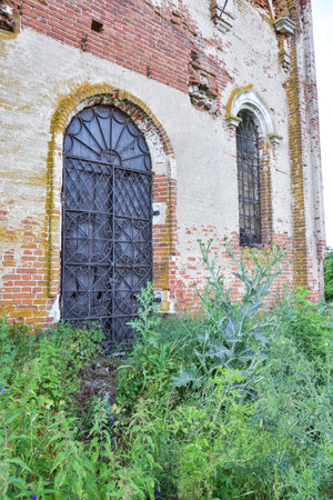 part of a ruined temple with a bell tower overgrown with grass against the background of a cloudy sky, framed by greenery, close-upの写真素材