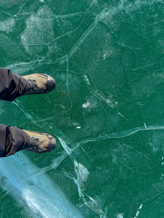A foot of tourist standing on the cracks surface of frozen lake Baikal in the winter season of Siberia, Russia. Traveler man foot standing on cracks surface of the natural ice in frozen water. Top angle view of feet standing on broken iceの写真素材