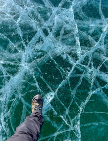 A foot of tourist standing on the cracks surface of frozen lake Baikal in the winter season of Siberia, Russia. Traveler man foot standing on cracks surface of the natural ice in frozen water. Top angle view of feet standing on broken iceの写真素材