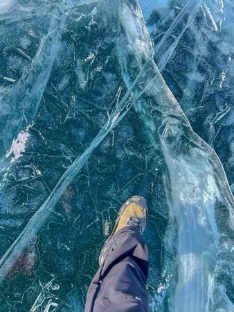 A foot of tourist standing on the cracks surface of frozen lake Baikal in the winter season of...