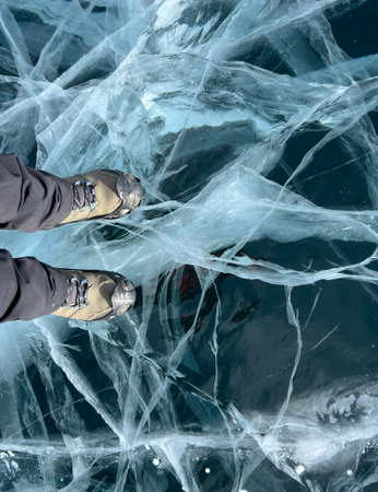A foot of tourist standing on the cracks surface of frozen lake Baikal in the winter season of Siberia, Russia. Traveler man foot standing on cracks surface of the natural ice in frozen water. Top angle view of feet standing on broken iceの写真素材