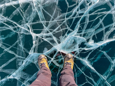 A foot of tourist standing on the cracks surface of frozen lake Baikal in the winter season of Siberia, Russia. Traveler man foot standing on cracks surface of the natural ice in frozen water. Top angle view of feet standing on broken iceの写真素材