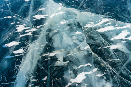 Abstract background of ice and cracks on the surface of frozen Lake Baikal. Spiderweb of cracks on slippery, smooth ice surface of a Baikal lake in Siberia (Russia). Cracks in the ice. Cracked ice on a frozen lake. The natural texture of winter ice with white bubbles and cracks on a frozen lake. Abstract bright background, flat layout, layout, top view. background. selective focus. Transparent dark blue ice of frozen Baikal lake with white cracks pattern. beautiful winter backgroundの写真素材