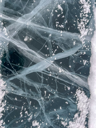 Abstract background of ice and cracks on the surface of frozen Lake Baikal. Spiderweb of cracks on slippery, smooth ice surface of a Baikal lake in Siberia (Russia). Cracks in the ice. Cracked ice on a frozen lake. The natural texture of winter ice with white bubbles and cracks on a frozen lake. Abstract bright background, flat layout, layout, top view. background. selective focus. Transparent dark blue ice of frozen Baikal lake with white cracks pattern. beautiful winter backgroundの写真素材