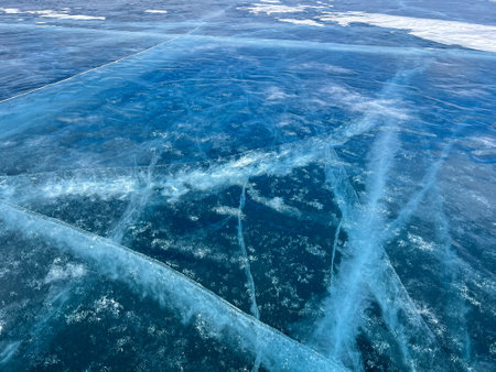 Abstract background of ice and cracks on the surface of frozen Lake Baikal. Spiderweb of cracks on slippery, smooth ice surface of a Baikal lake in Siberia (Russia). Cracks in the ice. Cracked ice on a frozen lake. The natural texture of winter ice with white bubbles and cracks on a frozen lake. Abstract bright background, flat layout, layout, top view. background. selective focus. Transparent dark blue ice of frozen Baikal lake with white cracks pattern. beautiful winter backgroundの写真素材