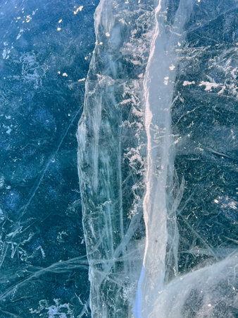 Abstract background of ice and cracks on the surface of frozen Lake Baikal. Spiderweb of cracks on slippery, smooth ice surface of a Baikal lake in Siberia (Russia). Cracks in the ice. Cracked ice on a frozen lake. The natural texture of winter ice with white bubbles and cracks on a frozen lake. Abstract bright background, flat layout, layout, top view. background. selective focus. Transparent dark blue ice of frozen Baikal lake with white cracks pattern. beautiful winter backgroundの写真素材