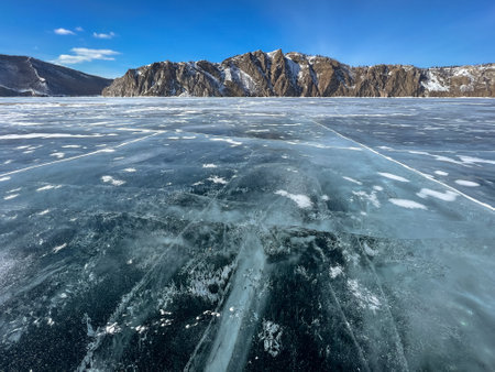 pure ice of the frozen lake Baikal against the background of mountainsの写真素材