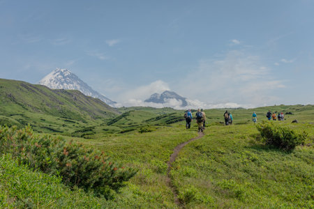 group of people walking along a dirt road towards a volcano. The road is in a grassy field with a volcano in the backgroundの写真素材