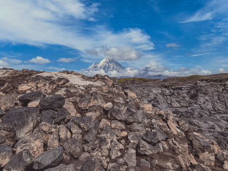 Lava fields with a volcano in the background. The mountain is covered in snow. The ground is rocky...
