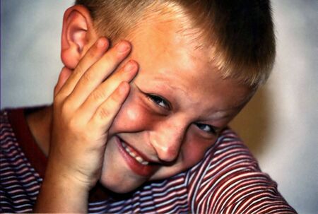 Portrait of boy with coy expression, hand to cheek.の写真素材