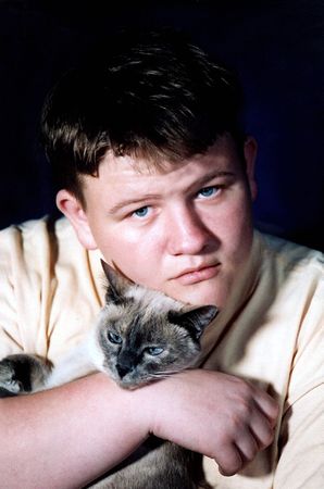 Vertical of teenage boy holding a Siamese cat under his chin.の写真素材