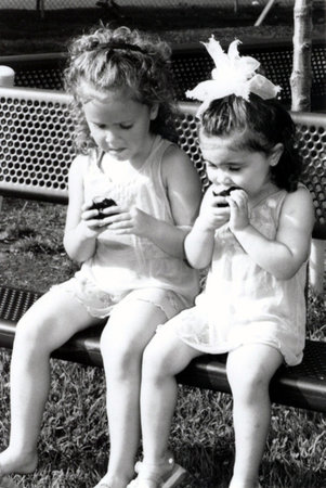Black and white of two sisters resting on a bench, eating fruit.の写真素材
