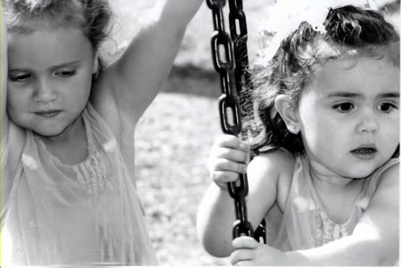Black and white of two sisters on a tire swing, not smiling.の写真素材
