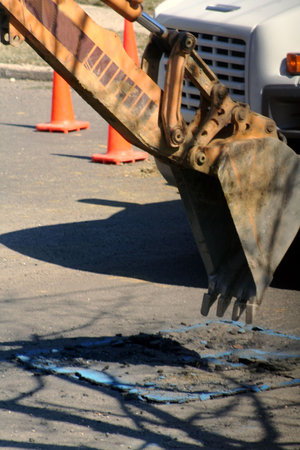 Backhoe preparing to dig into asphalt street.