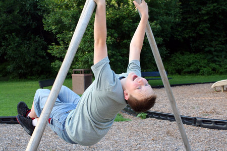Teenage boy hanging from playground apparatus.