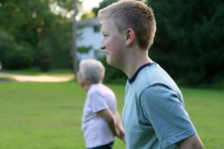 Outdoor portrait of serious teenage boy with grandmother in background.の写真素材