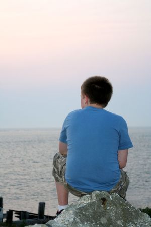 Pensive teenage boy looking out at the ocean at sunset.の写真素材