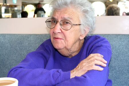 Senior citizen woman sitting in a booth with a cup of coffee at a diner.の写真素材