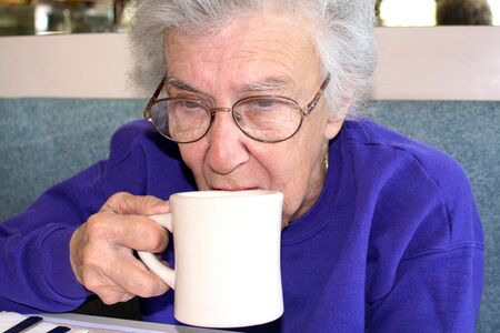 Senior citizen woman drinking from a cup of coffee at a diner.の写真素材