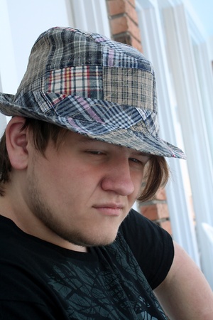 Closeup of a serious teenage boy with squinted eyes, wearing a plaid hat in an outdoor setting.の写真素材