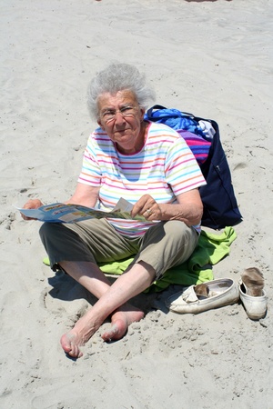 Senior citizen woman sitting on a beach reading a brochure.の写真素材