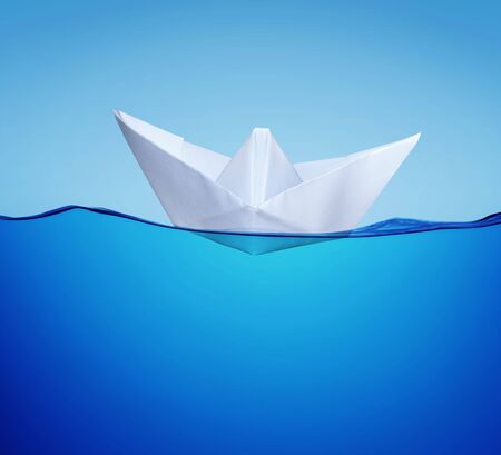 white paper toy-ship on the blue water in half face viewの写真素材