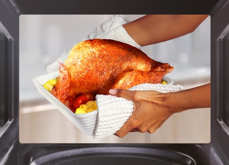 hands of woman is taking out  turkey with potato from ovenの写真素材
