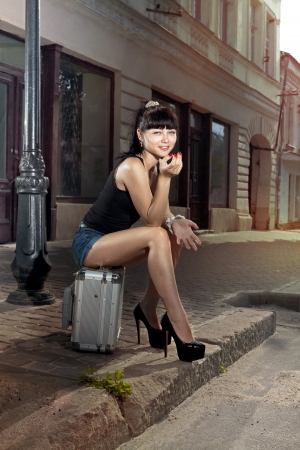 woman sits on suitcase near road in the small ancient cityの写真素材