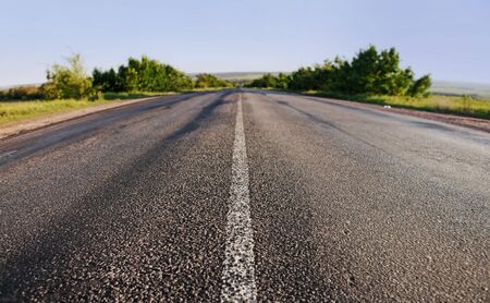 asphalt road through the green field on blue sky in summer dayの写真素材
