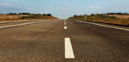 asphalt road through the field on blue sky in summer dayの写真素材