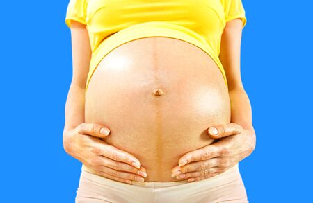 closeup stomach and hands of pregnant woman on blue backgroundの写真素材