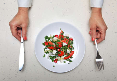 hands with kitchen flatware and fresh vegetables sliced in white plateの写真素材