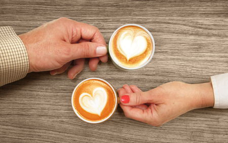 hands of lovers which hold cups of coffee on tableの写真素材