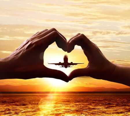 Hands of lovers in the form of heart, which against the background of the sky with the taking-off planeの写真素材