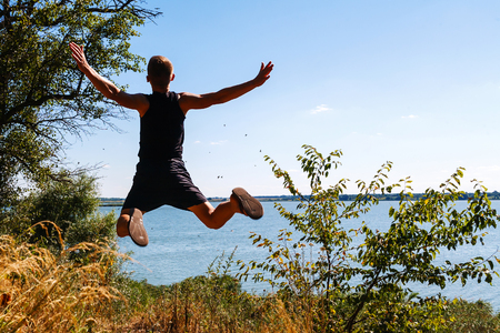 The boy jumps into the river from the high bank. Back view.の写真素材