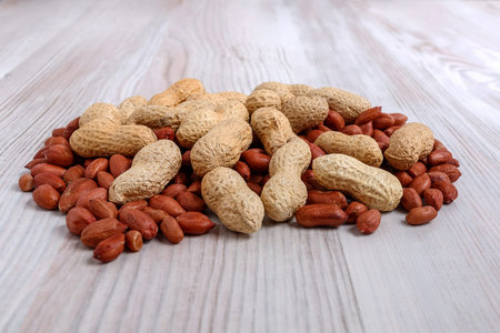 A heap of unpeeled and peeled peanuts on a light kitchen table close-up.