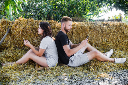 A young beautiful white couple, a girl and her bearded boyfriend, sit on a straw back to back and...