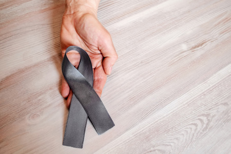 A woman's hand hold a gray ribbon of awareness of Parkinsons disease. As a symbol of Parkinsons Day.の写真素材