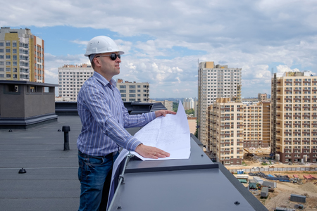 Foreman or developer in white helmet and sunglasses on roof are looking at the project on the construction site. Summer, cloudy sky.の写真素材